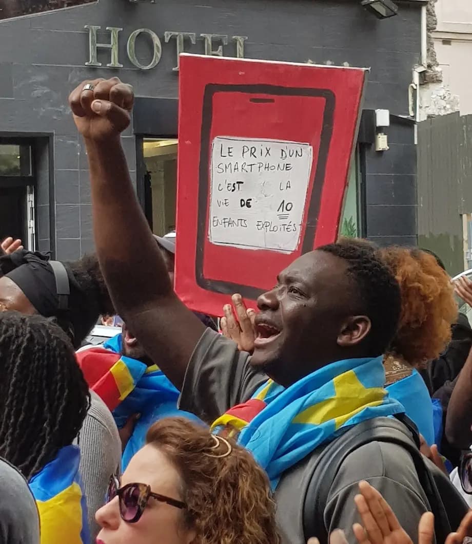 Manifestation avec une personne tenant une pancarte sur laquelle on peut lire : "Le Prix d'un smartphone, c'est la vie de 10 enfants exploités"